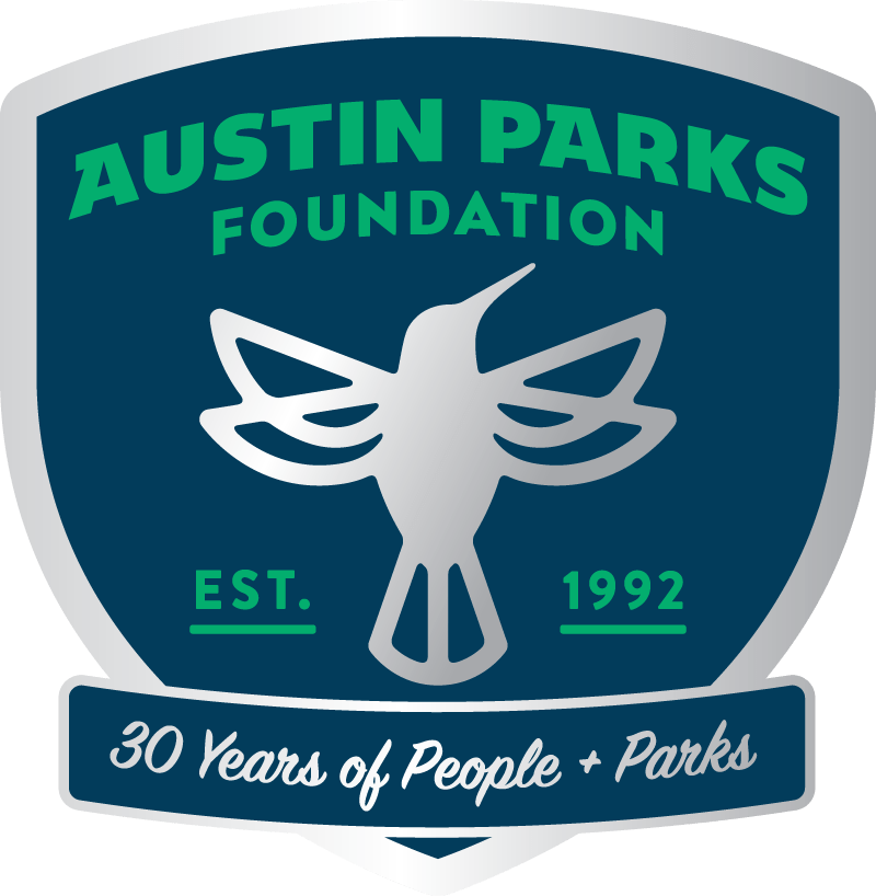 Navy blue badge outlined with silver. Inside the badge, there is a silver icon of a hummingbird and green text reading 'Austin Parks Foundation, Established 1992; 30 years of people plus parks'.