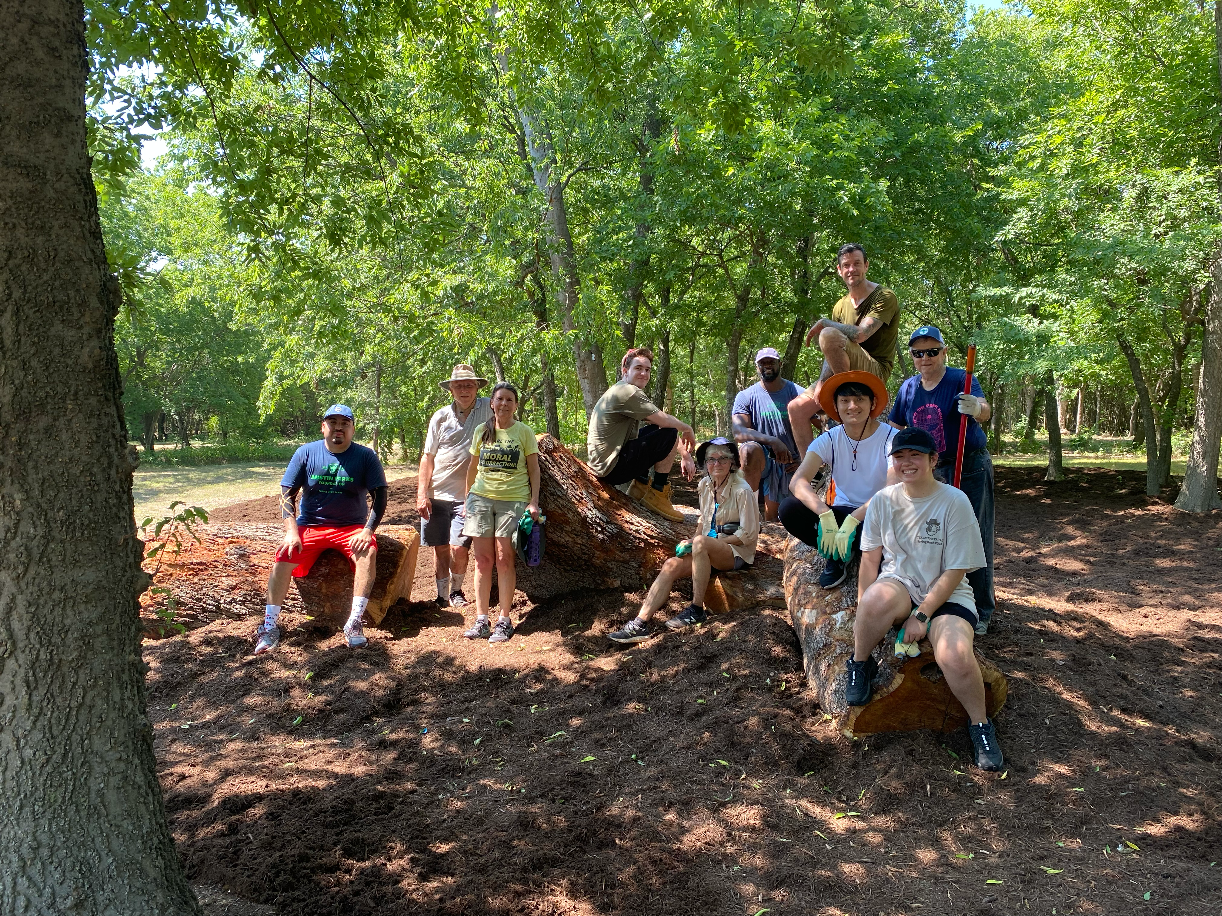 Volunteers sit atop logs after mulching and sealing Kendra Page Nature Playground