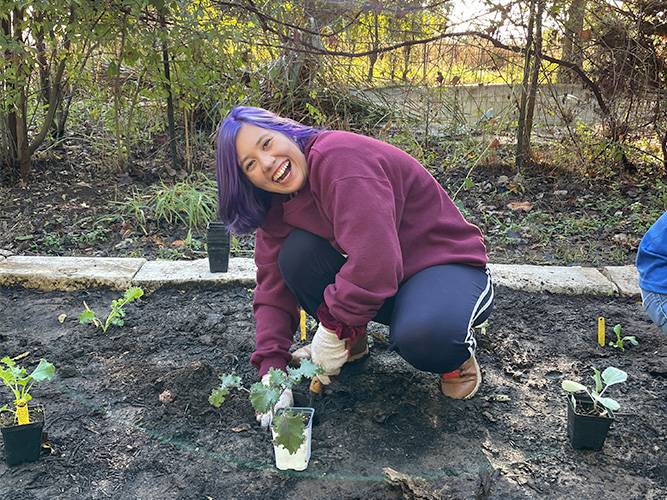 A purple-haired volunteer posing with a plant in a garden bed for It's My Park Day Fall 2022